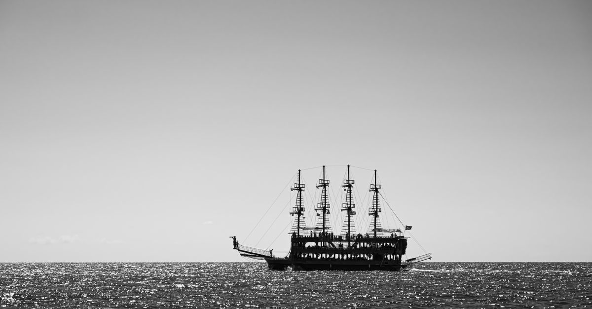 Black and white photo of a sailing ship on the shimmering ocean horizon.